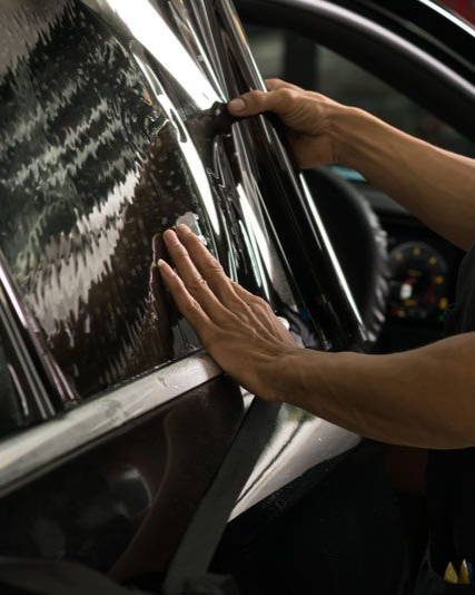 Person applying tinted film to a car window, hands smoothing the dark material.