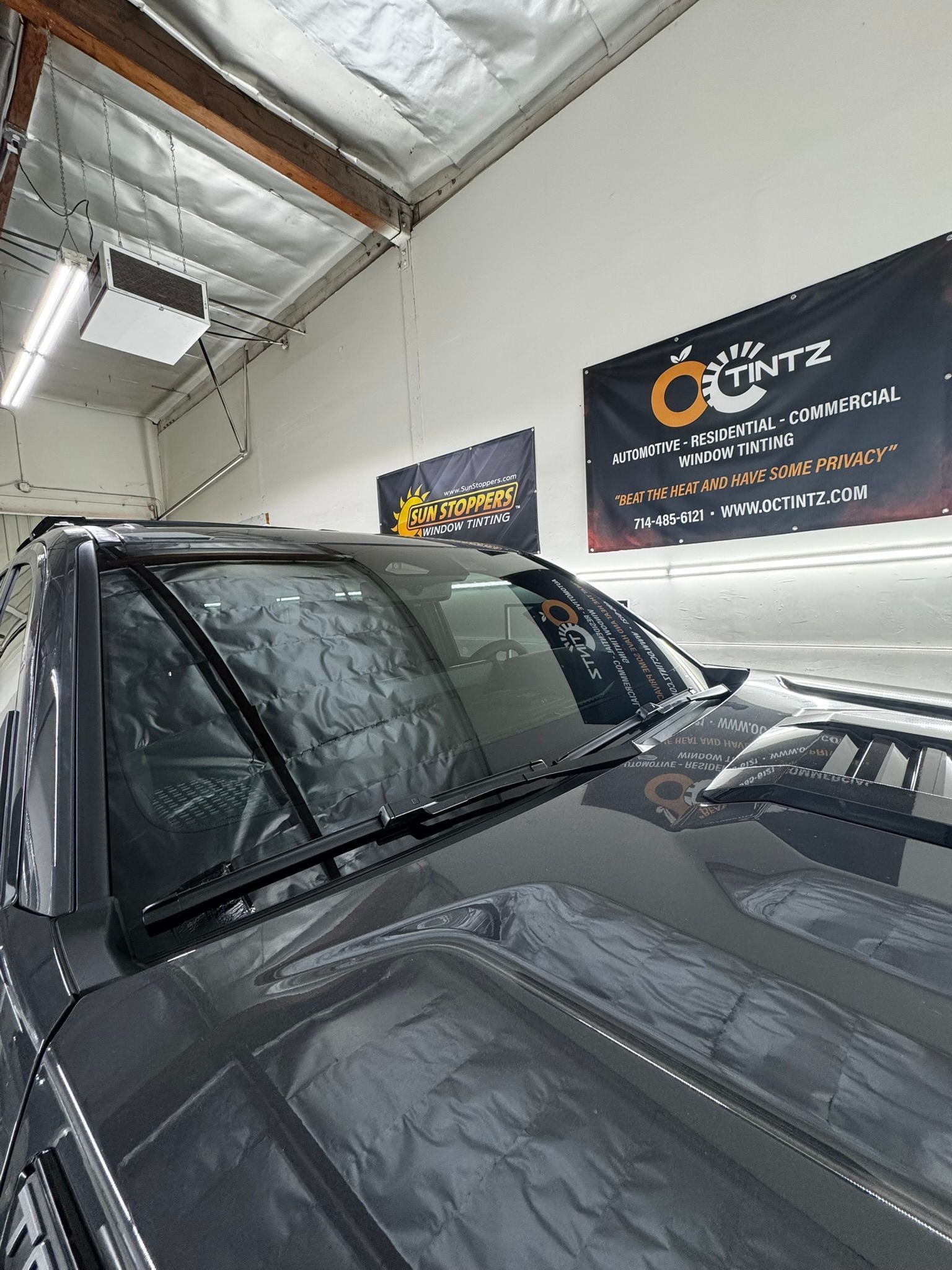 A person applying tinted film to a car window in a garage.