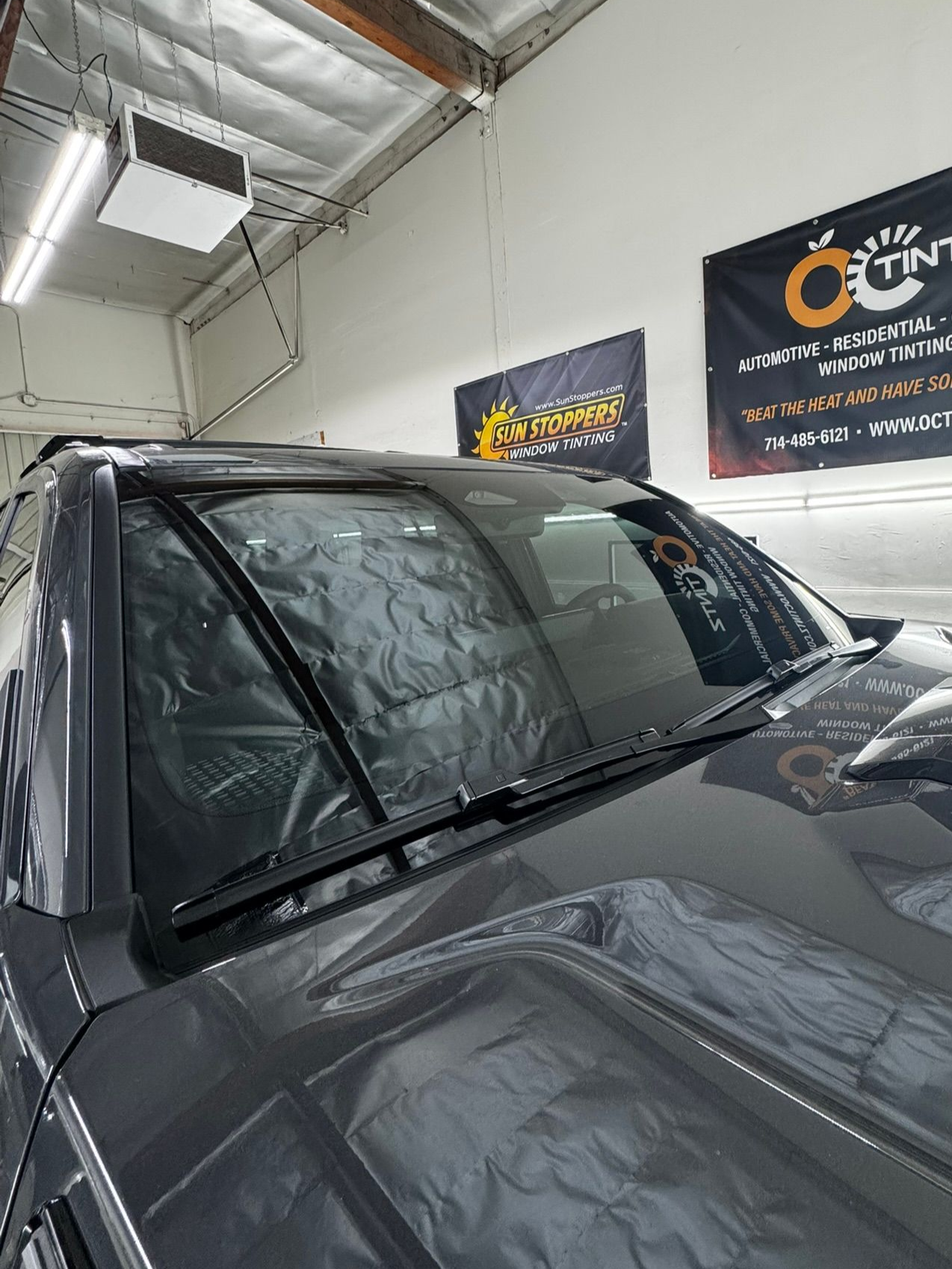 Person in black gloves applying film to a car window with spray, in a garage.