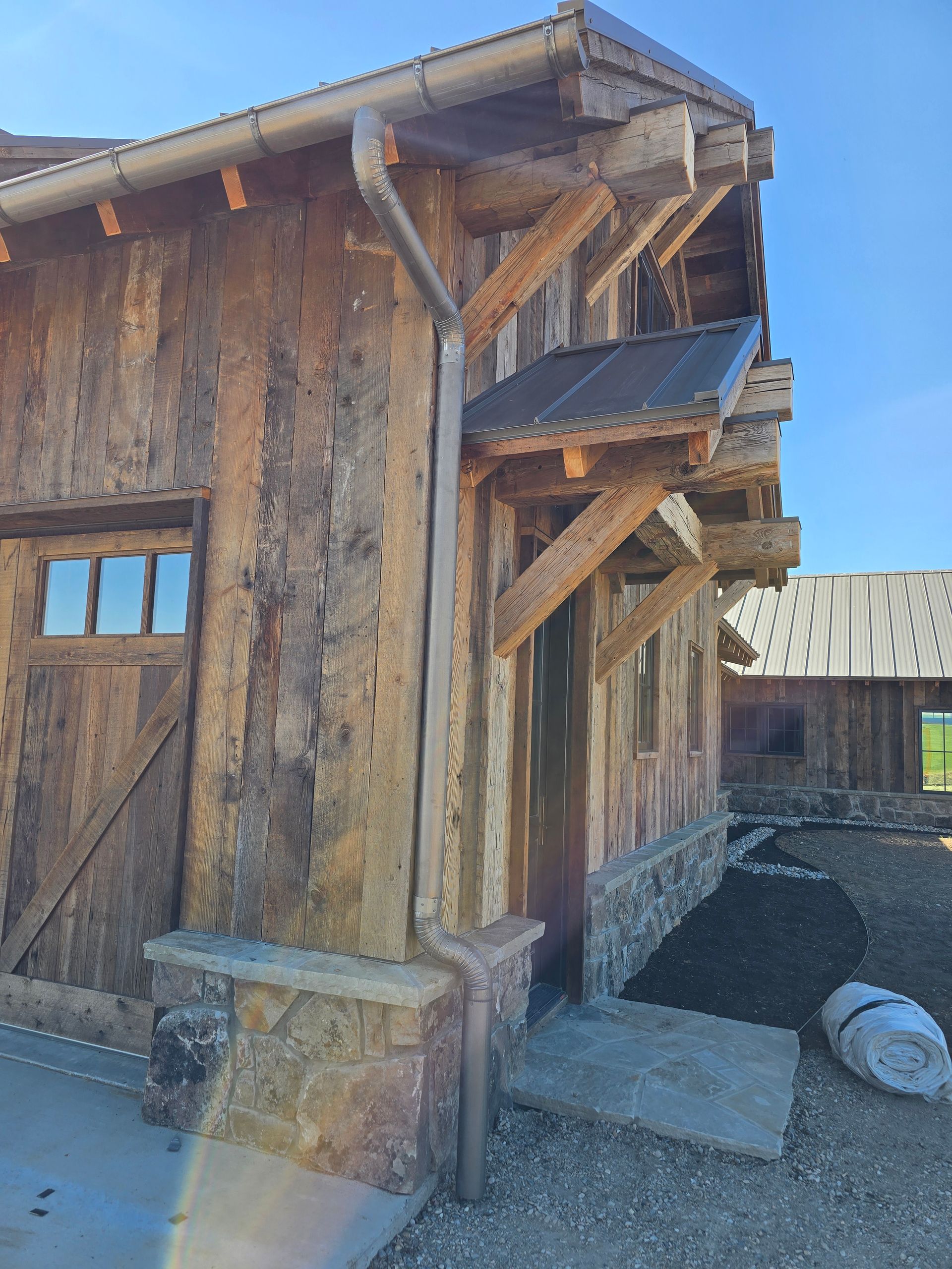 Rustic wooden building exterior with a metal roof, stone base, and heavy timber accents under a clear blue sky.