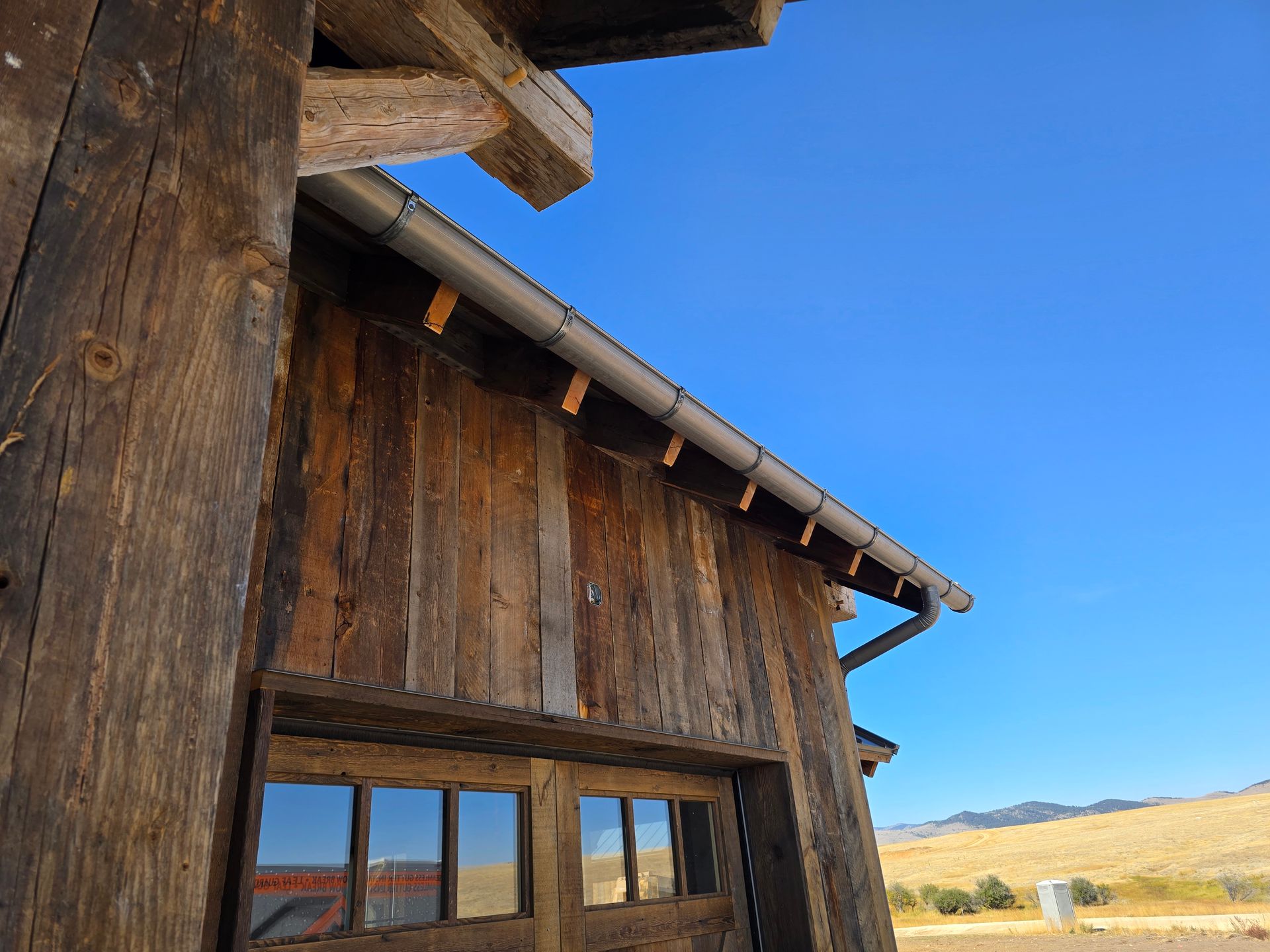 Rustic wooden building exterior with a metal gutter, showing timber-frame details under a clear blue sky.