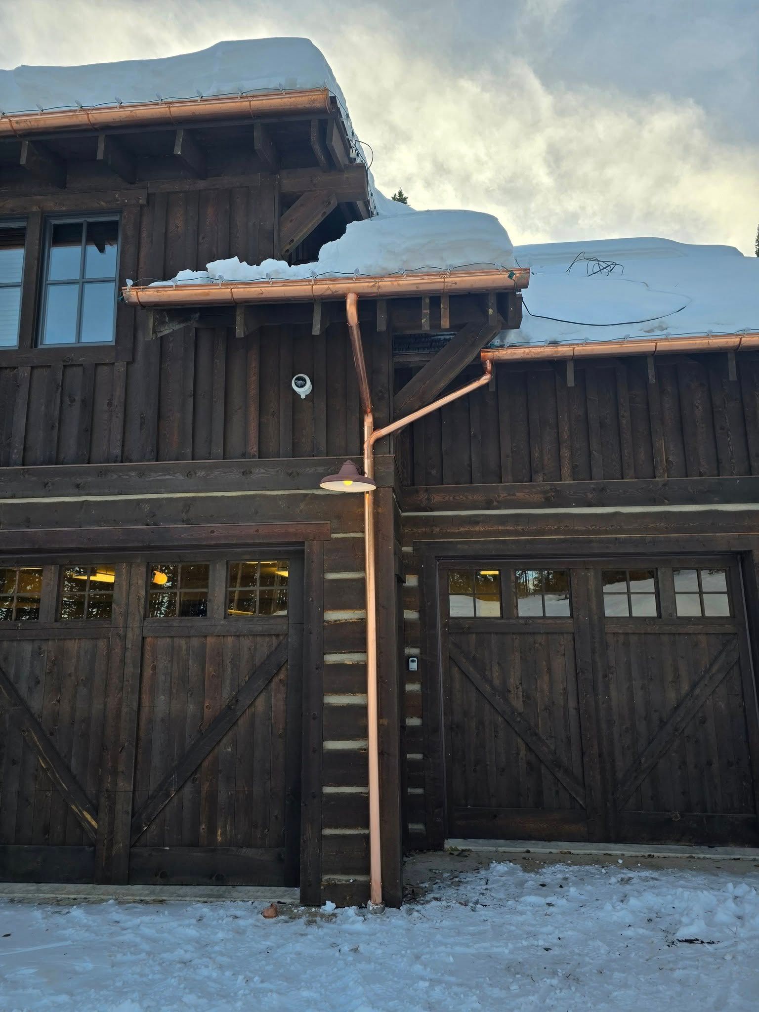 Rustic wooden garage building in winter with snow on the roof and copper gutters.