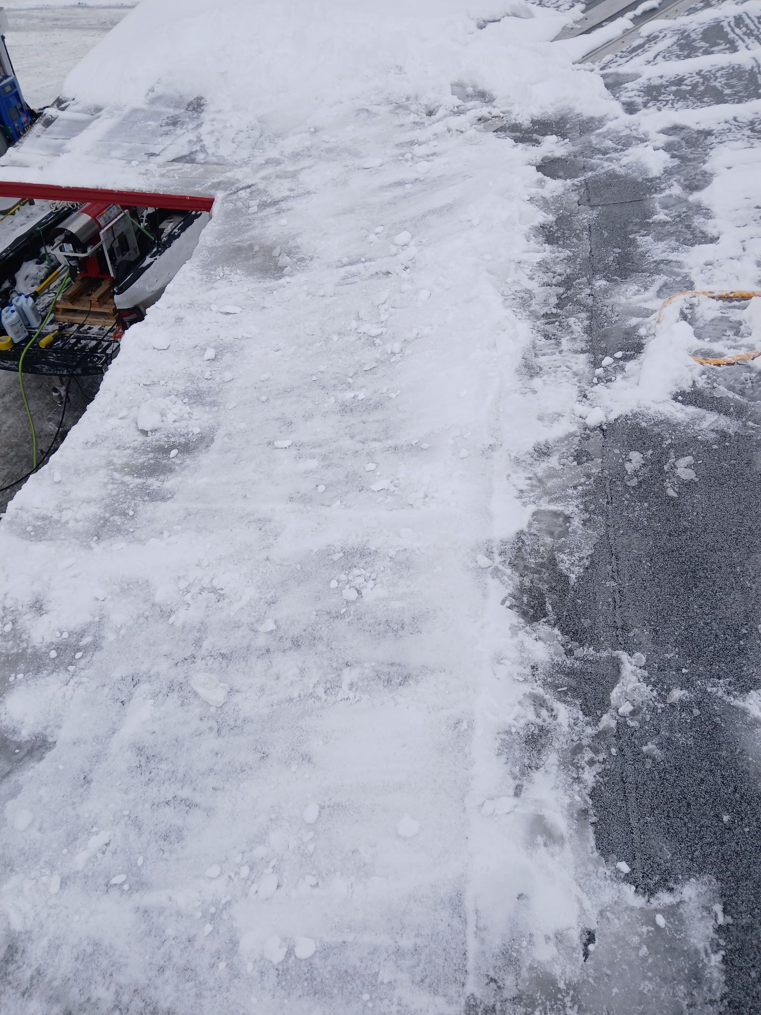 A red-framed snowblower sitting on a snowy driveway, clearing a path on the icy, gravel-covered surface.