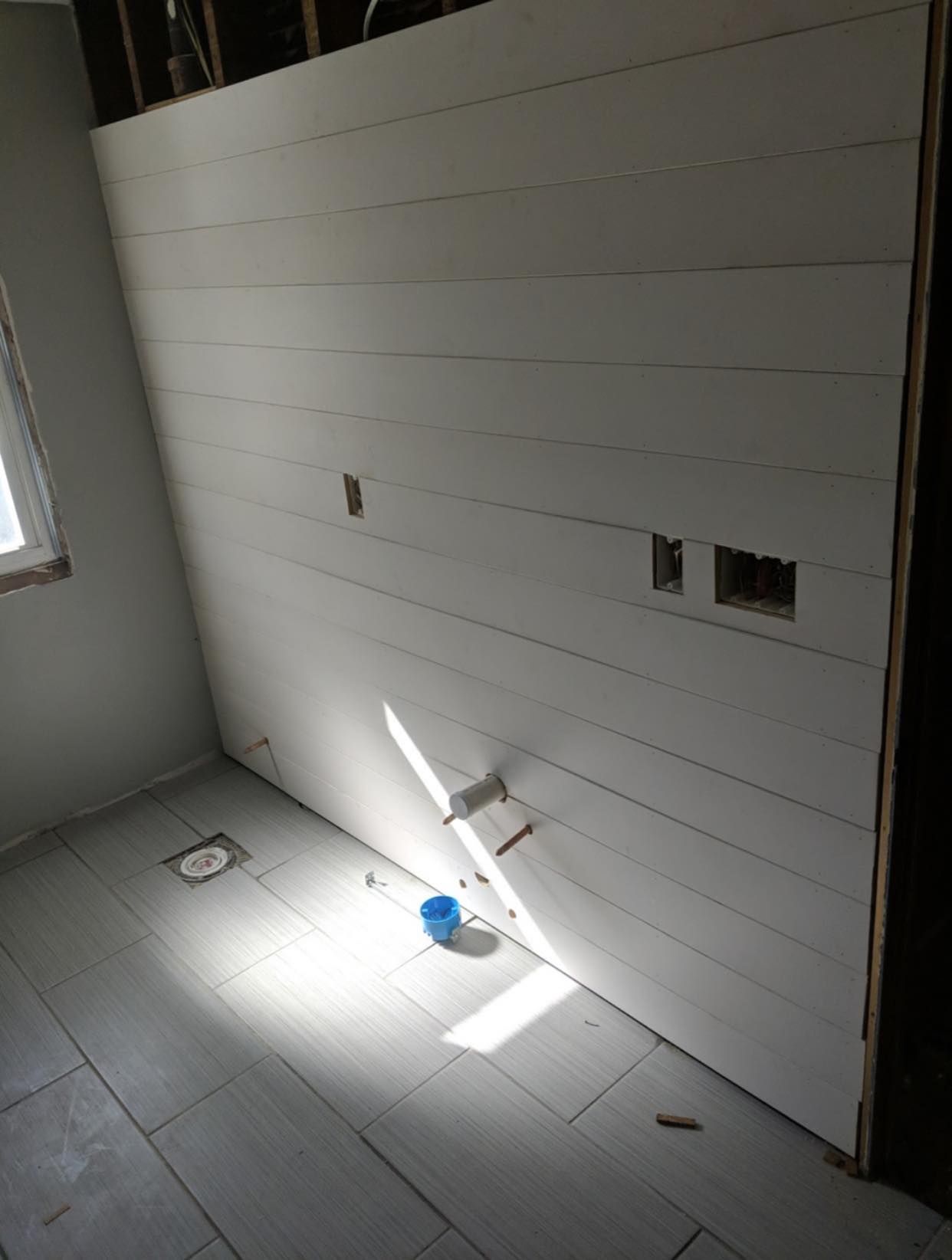 White shiplap wall in a room with light gray tiled floor. Construction in progress.