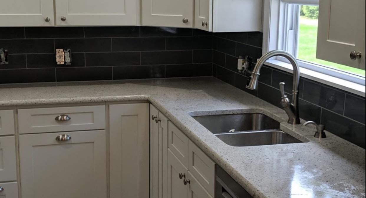 White kitchen cabinets with a granite countertop, sink, and dark gray backsplash.