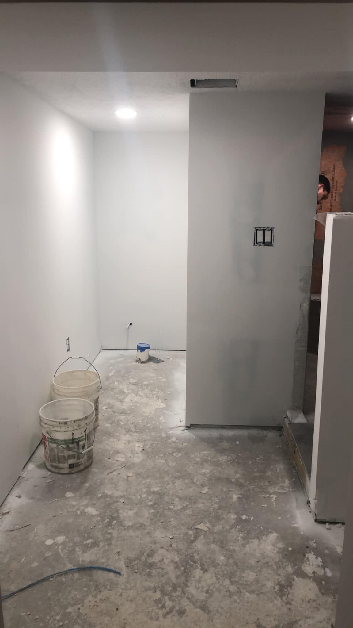 A room under construction with white walls, a concrete floor, and buckets.