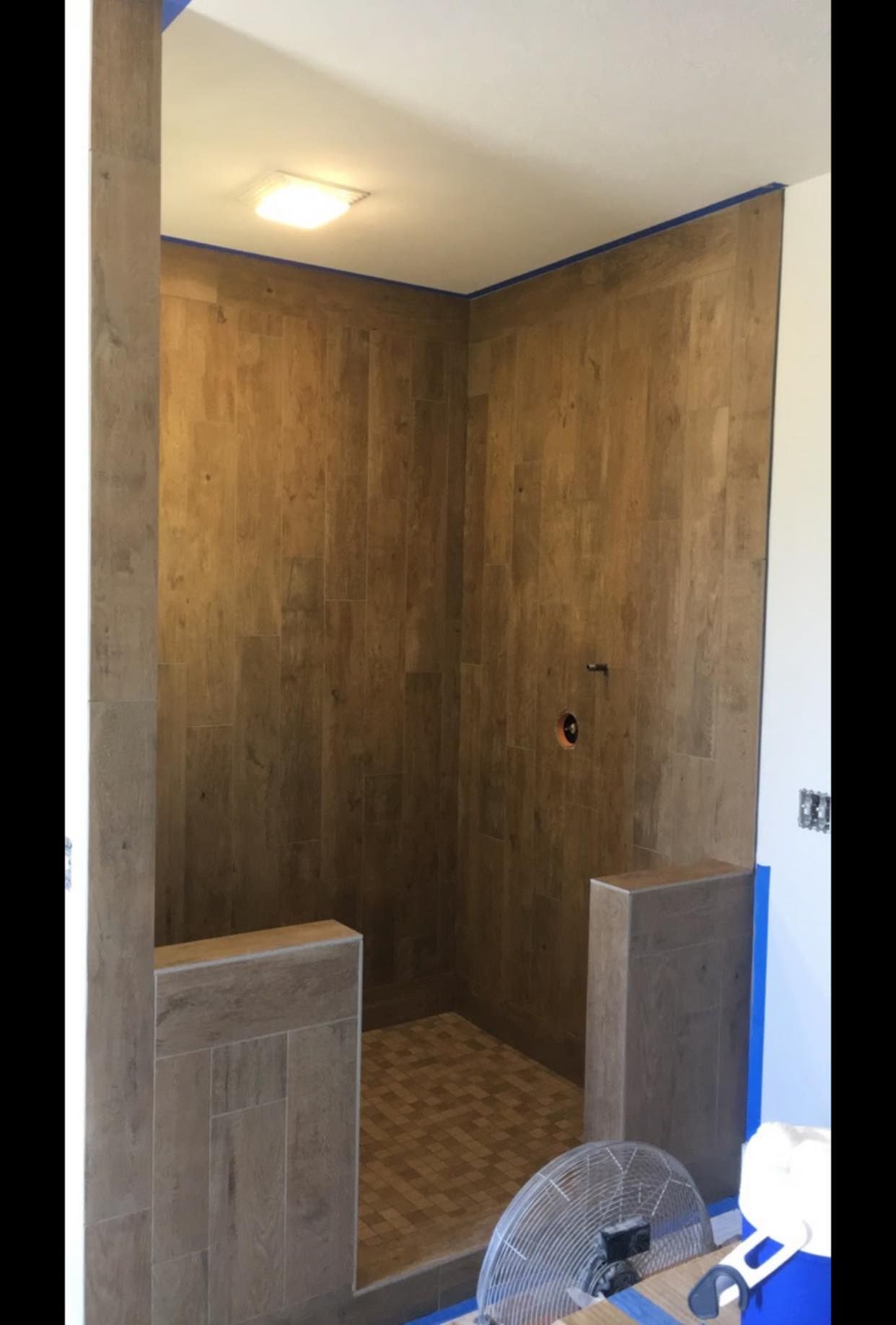 Newly tiled shower with wood-look tiles on walls and floor. Low entry with small tile knee walls.
