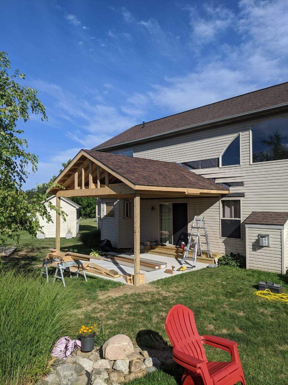 Construction of a covered patio attached to a house with a shingled roof; exterior setting, sunny day.