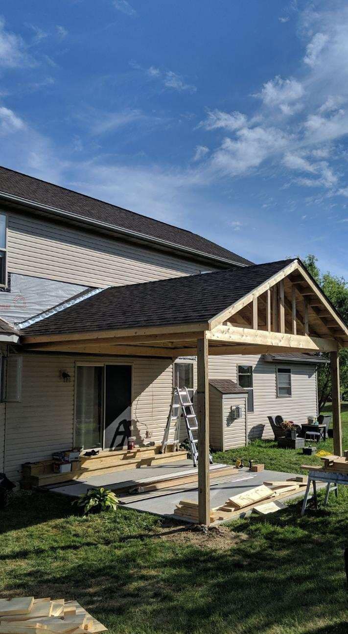 Backyard with a partially built wooden patio cover attached to a house with gray shingles and sliding door.