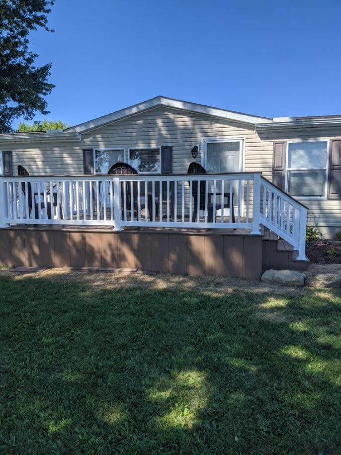 A house with a white deck, brown siding, and grass in the foreground under a clear sky.