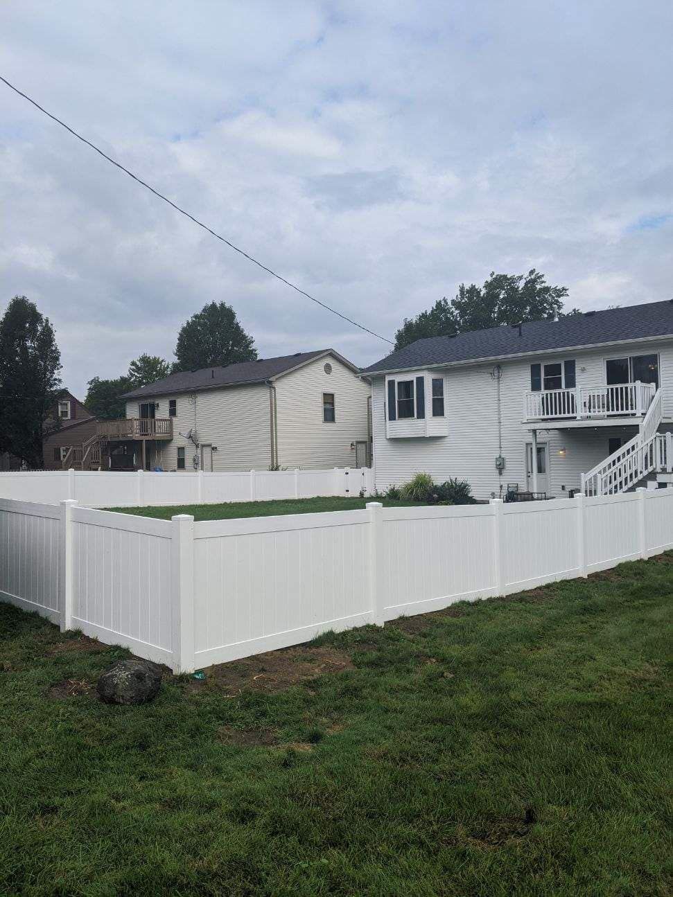 White vinyl fence surrounding a grassy yard with houses in the background under a cloudy sky.