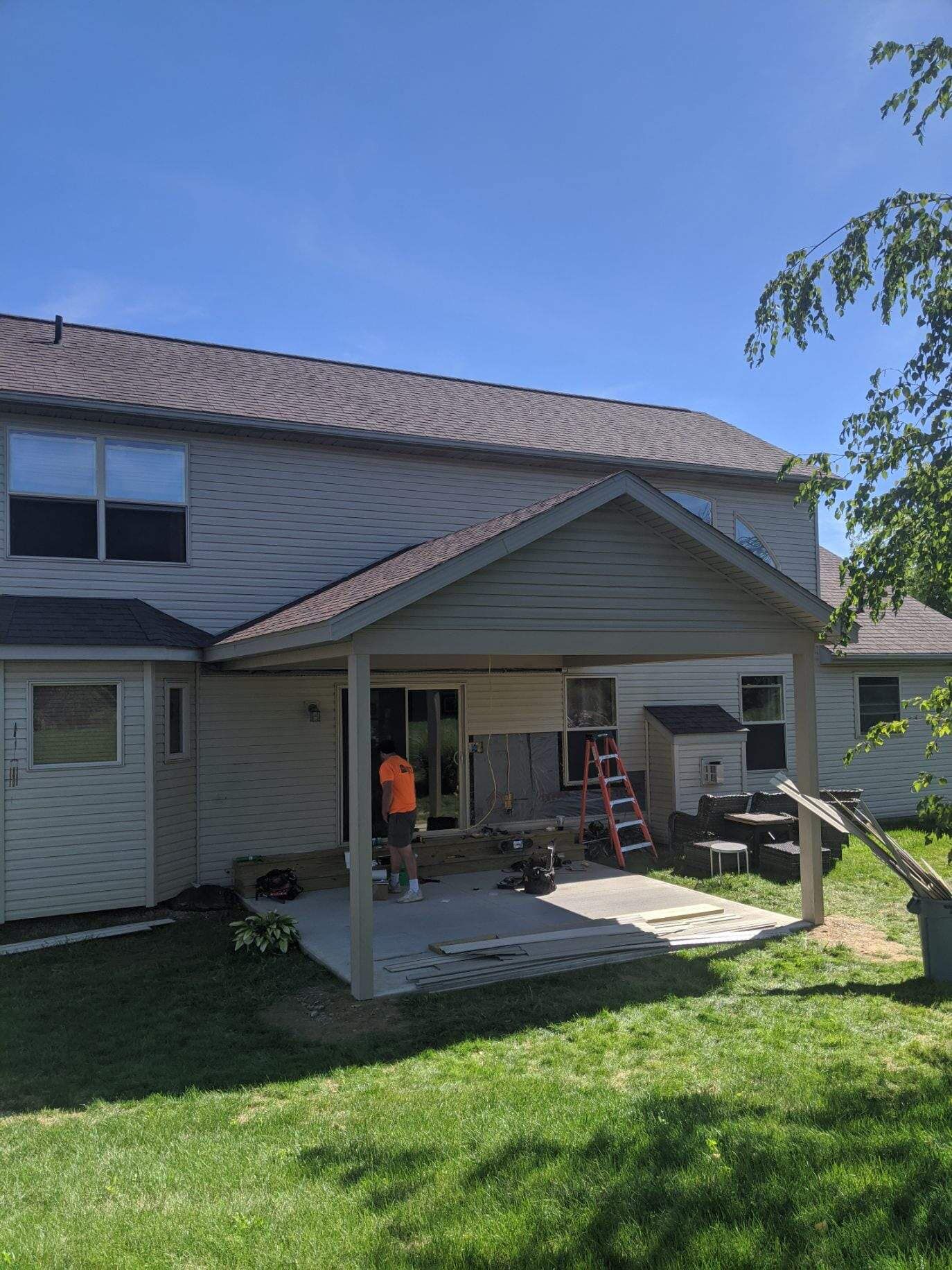 Back of a two-story beige house with a covered patio under construction. A person is working on the patio.