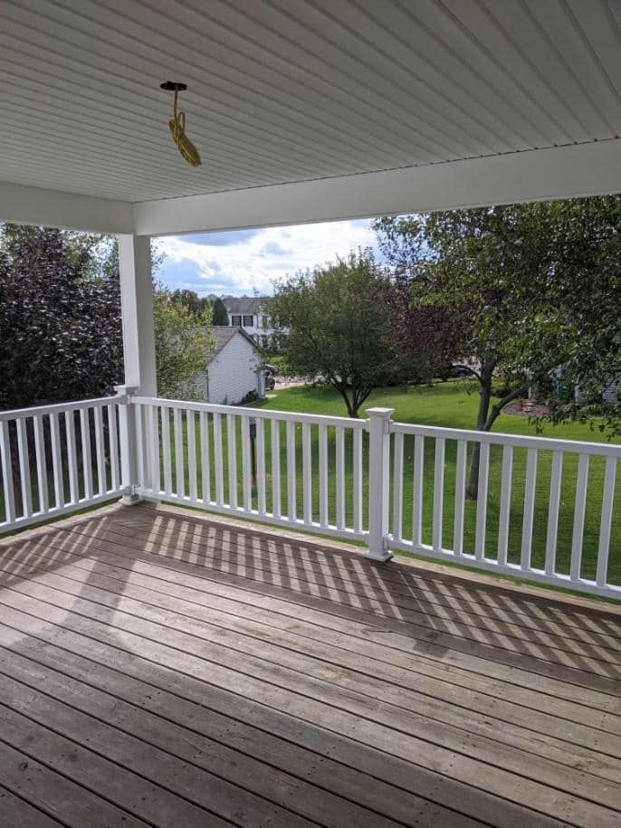 Deck with white railing and view of a green lawn and trees.