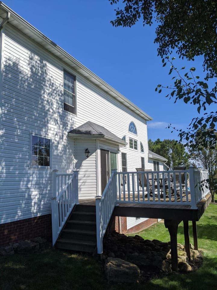 White house with a wooden deck, stairs, and a clear blue sky.