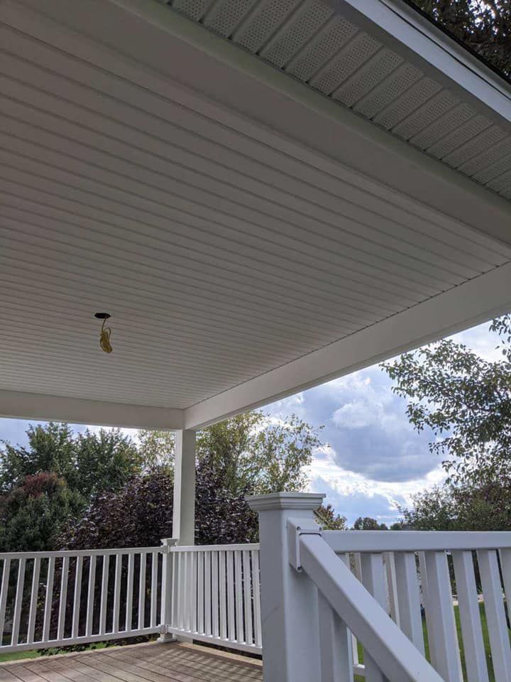 White porch ceiling and railing with a view of trees and cloudy sky.
