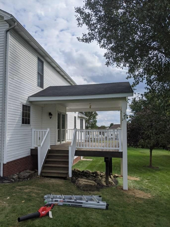 White house with a covered wooden deck and steps leading down to a grassy yard.