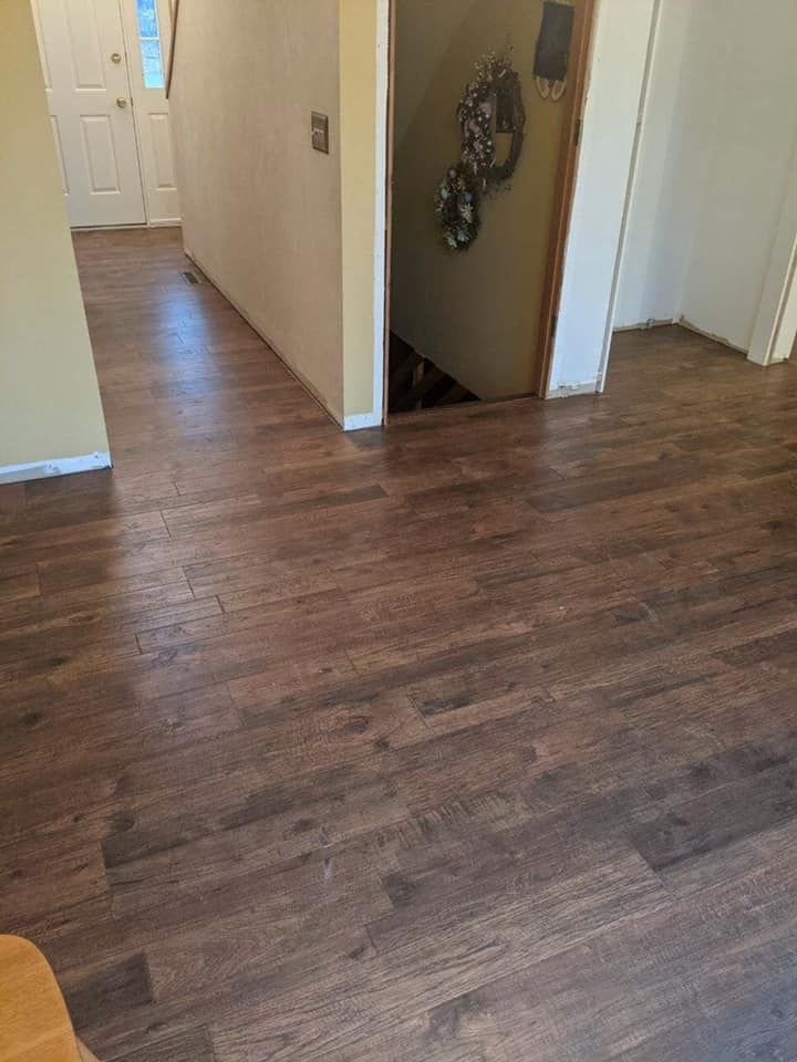 Dark wood-look flooring extends through a hallway and into a doorway. Beige walls and a staircase are visible.