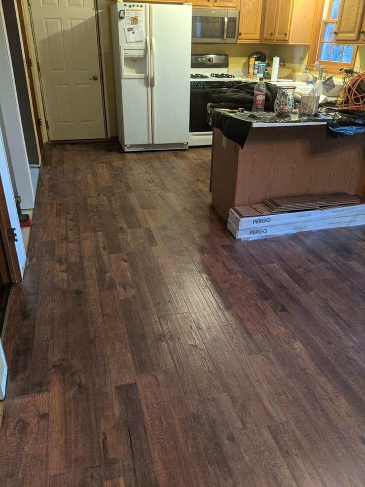 Dark wood flooring in a kitchen with a white refrigerator, black stove, and an island with supplies.