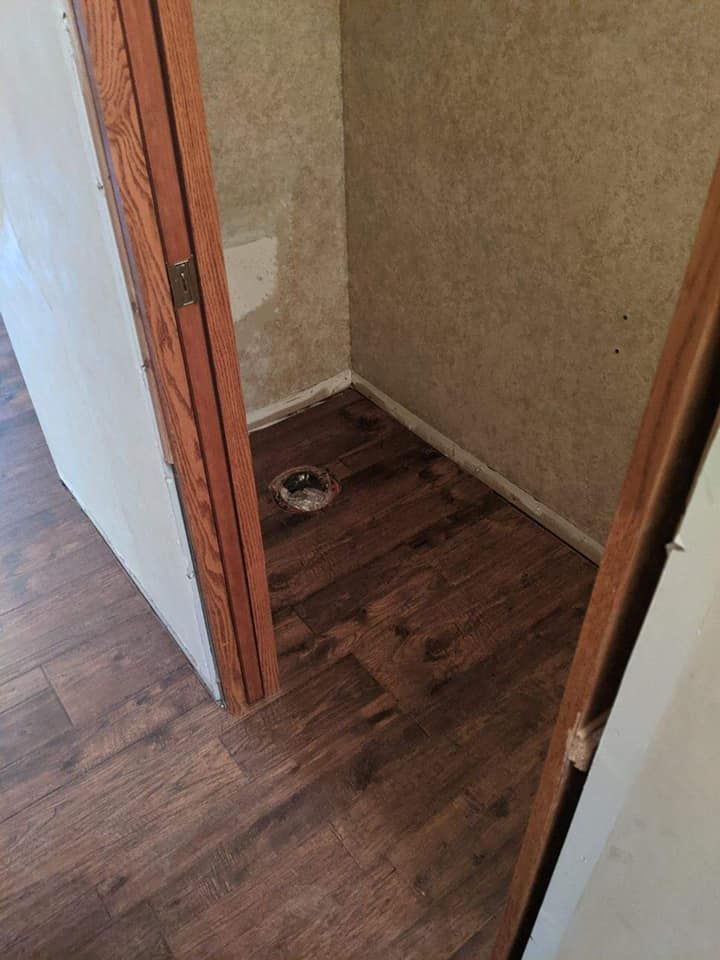 An empty closet with a toilet flange on a wood floor, beige walls, and brown door frames.