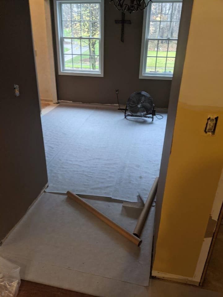 Room with protective covering on the floor, windows, and a fan. Construction in progress.