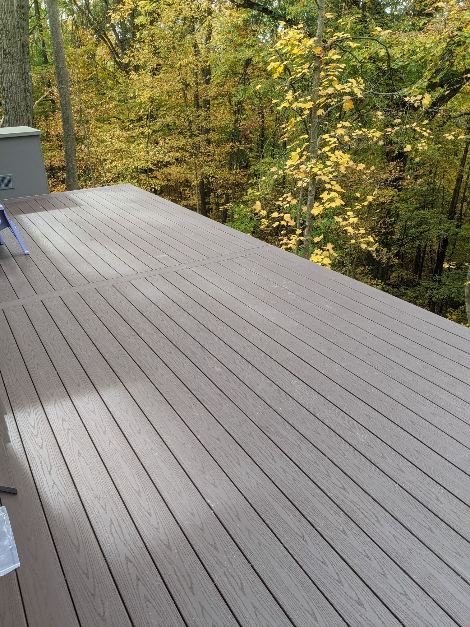 Wooden deck with gray planks surrounded by trees with yellow and green leaves.
