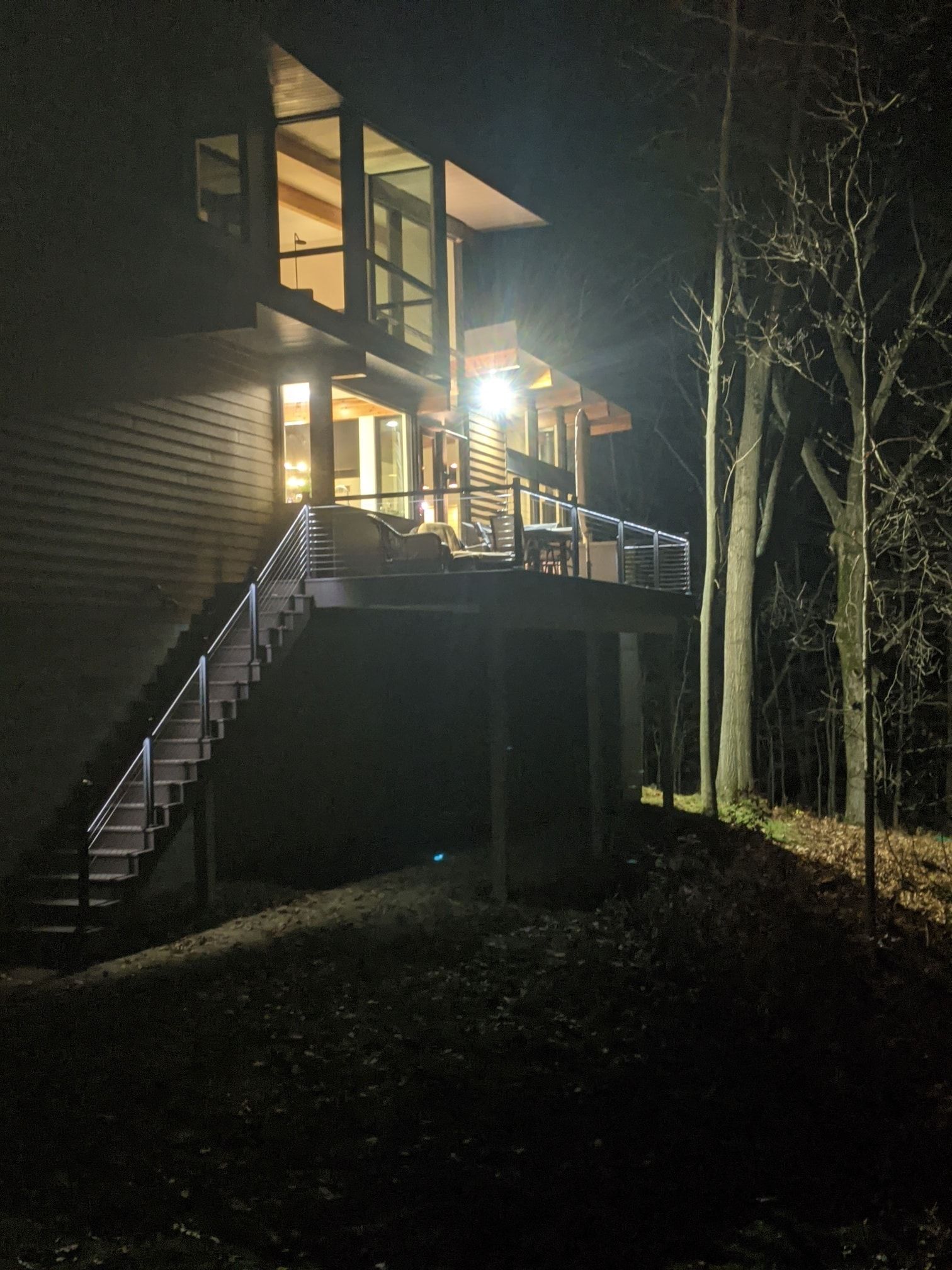 Lit-up house at night with stairs and deck. String lights illuminate the stairs. Trees stand in the background.