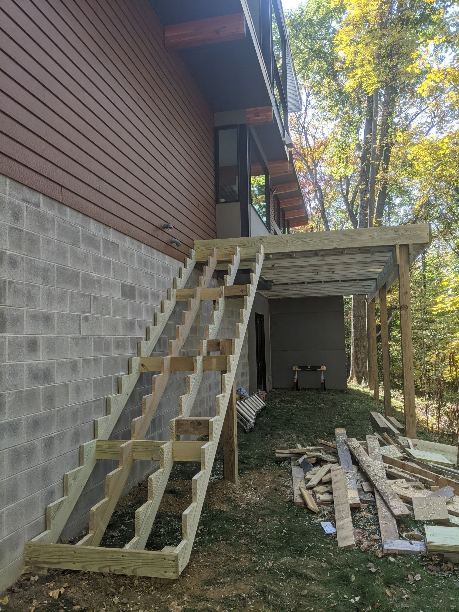 Wooden staircase under construction, leading up to a deck attached to a building with cinder block foundation.