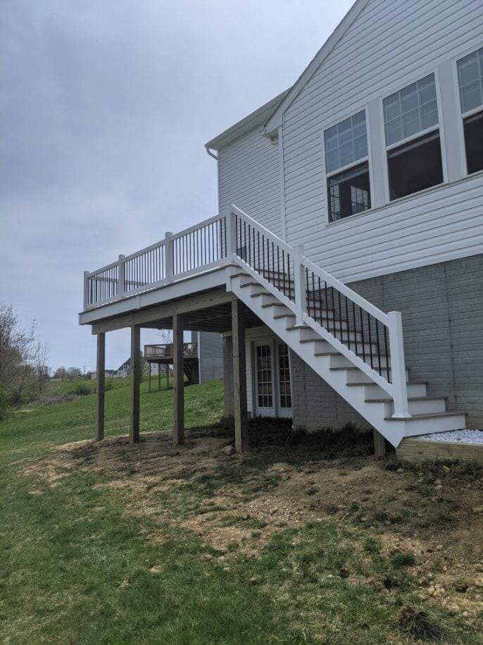 Elevated wooden deck attached to a two-story house with stairs leading to a backyard.