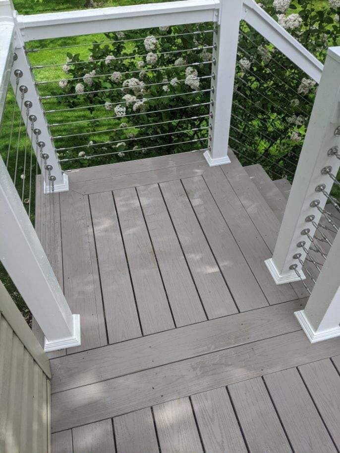 Grey composite deck with white railings and cable infill, outdoors.