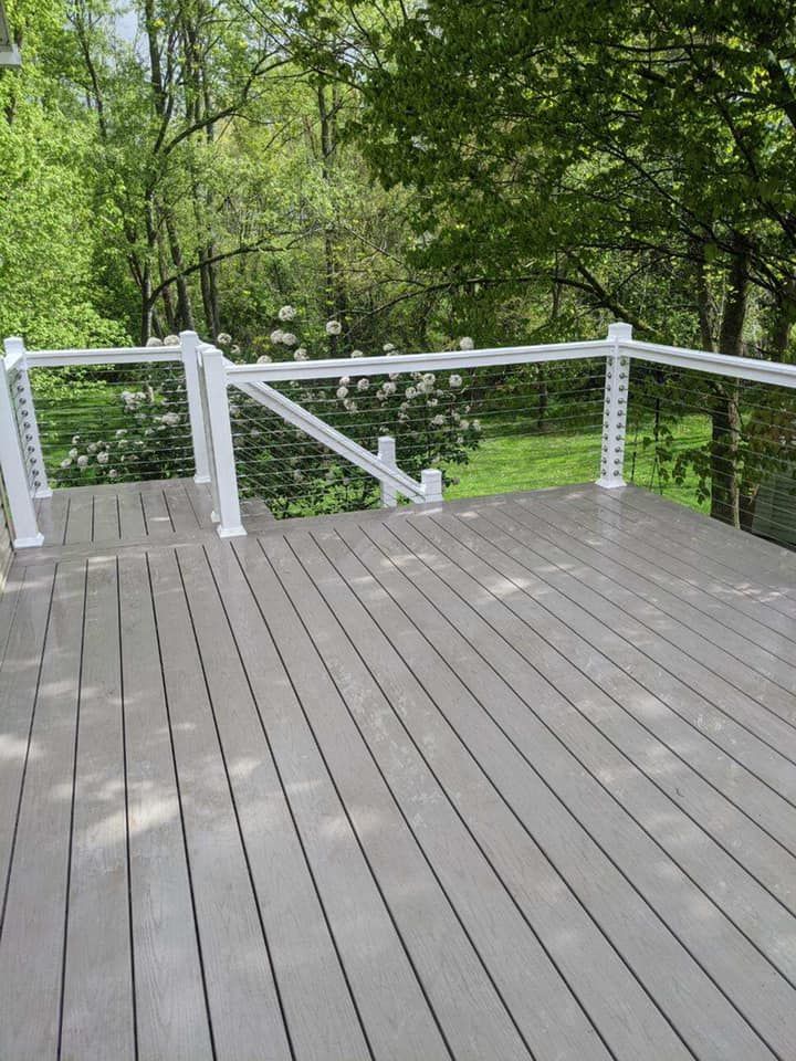 Wooden deck with white railing overlooking a green yard and trees.