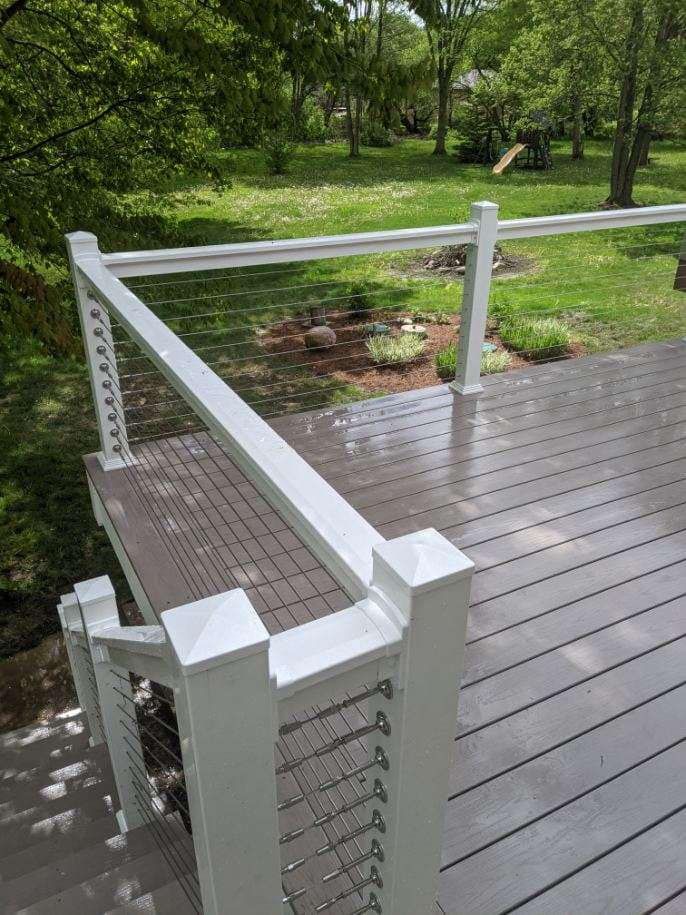 White deck railing with metal cable, leading to a wooden deck and green yard.