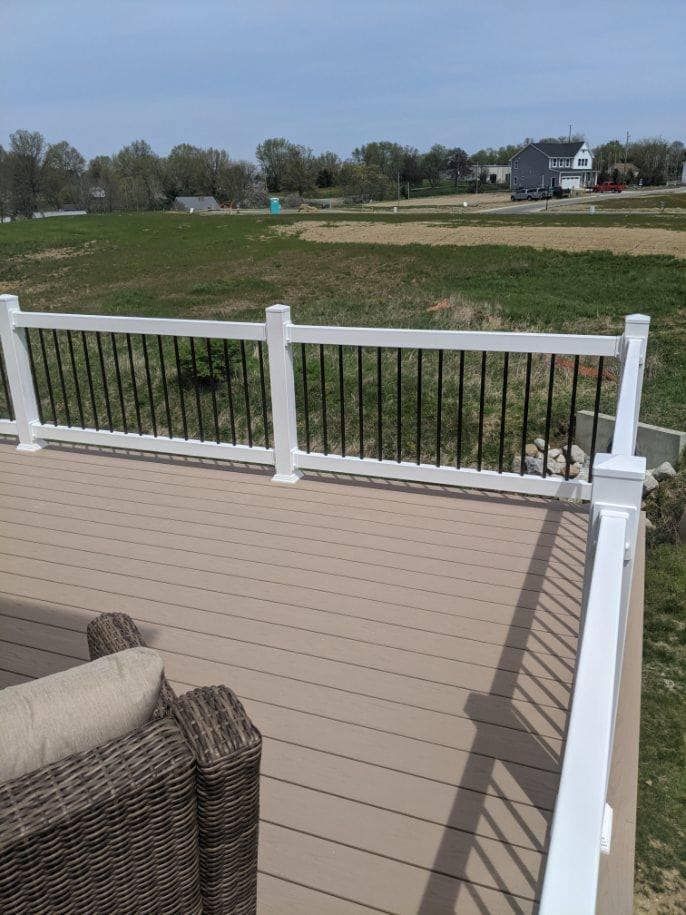 Composite deck with white posts, black railings, and a field in the background.