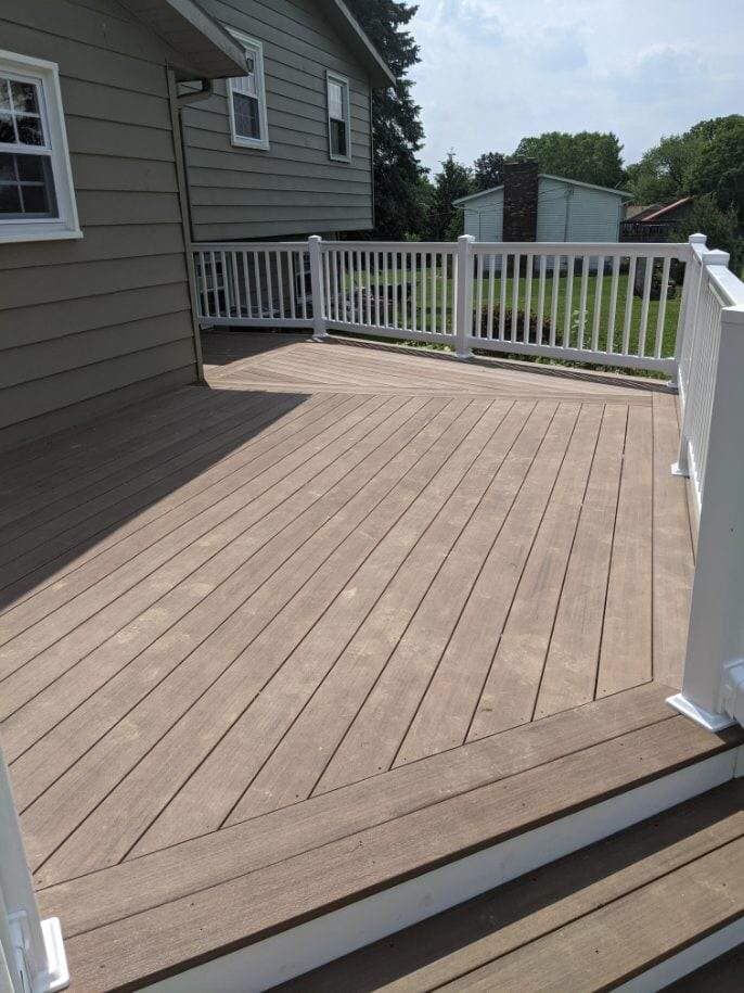 A wooden deck with a white railing attached to a beige house, sunny outdoor setting.