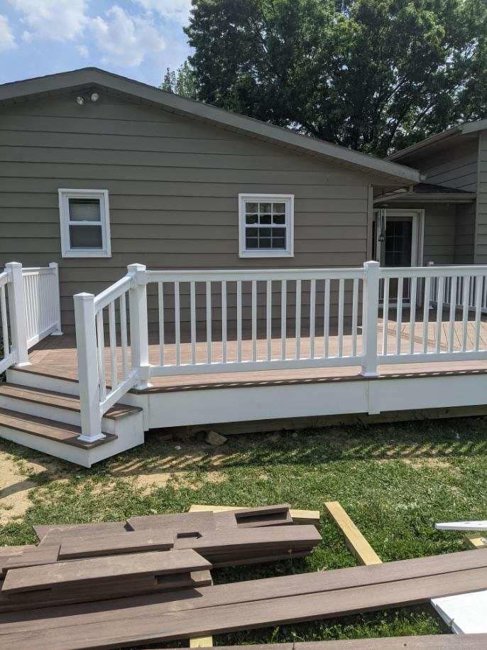 A newly built deck with white railings and brown composite decking boards against a tan house with windows.