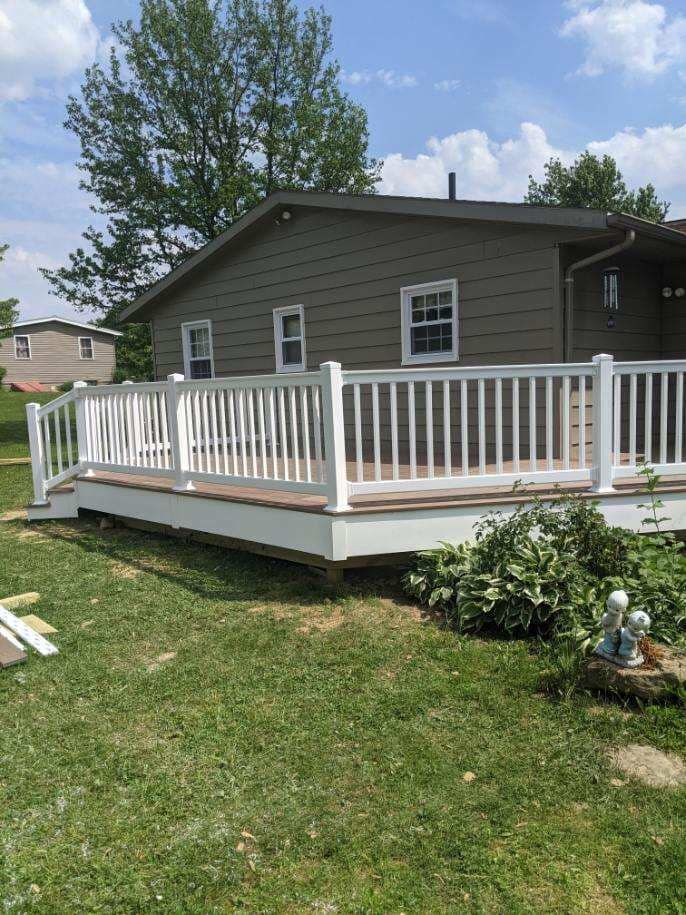 White-railed deck with light brown flooring, attached to a house with green siding, on a grassy lawn.