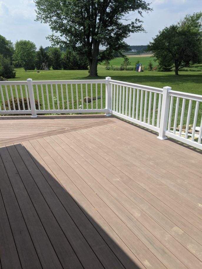 Wooden deck with white railing overlooking a grassy yard and trees under a sunny sky.