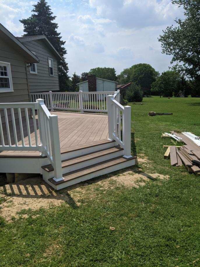 Finished deck with white railings, brown steps, and composite decking in a grassy yard next to a house.