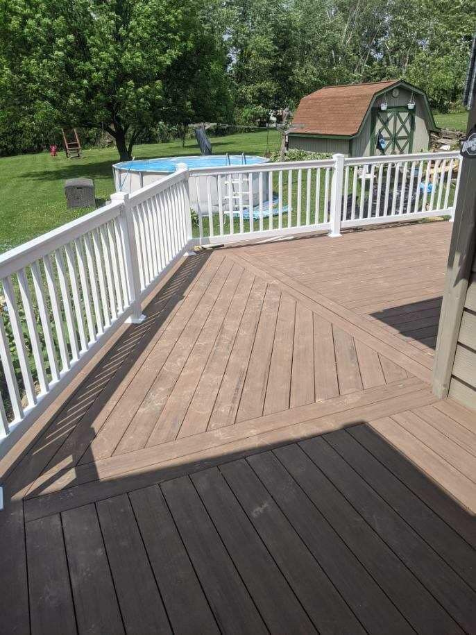 A brown composite deck with white railings overlooks a pool and a small shed in a backyard.