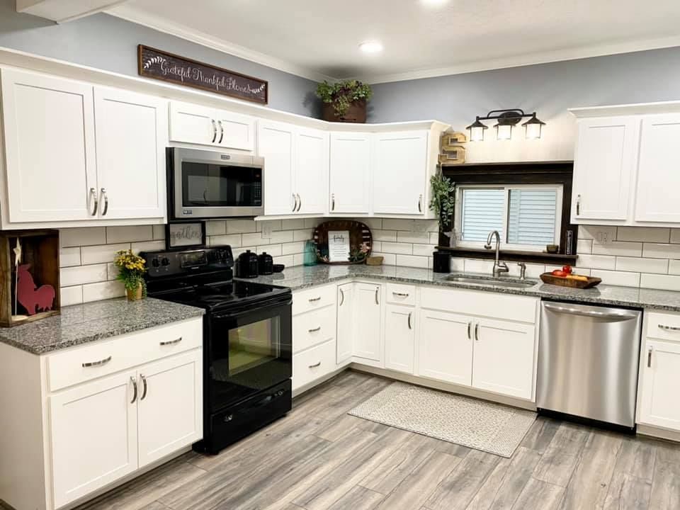 White kitchen with black appliances, gray countertop, and light gray floors.
