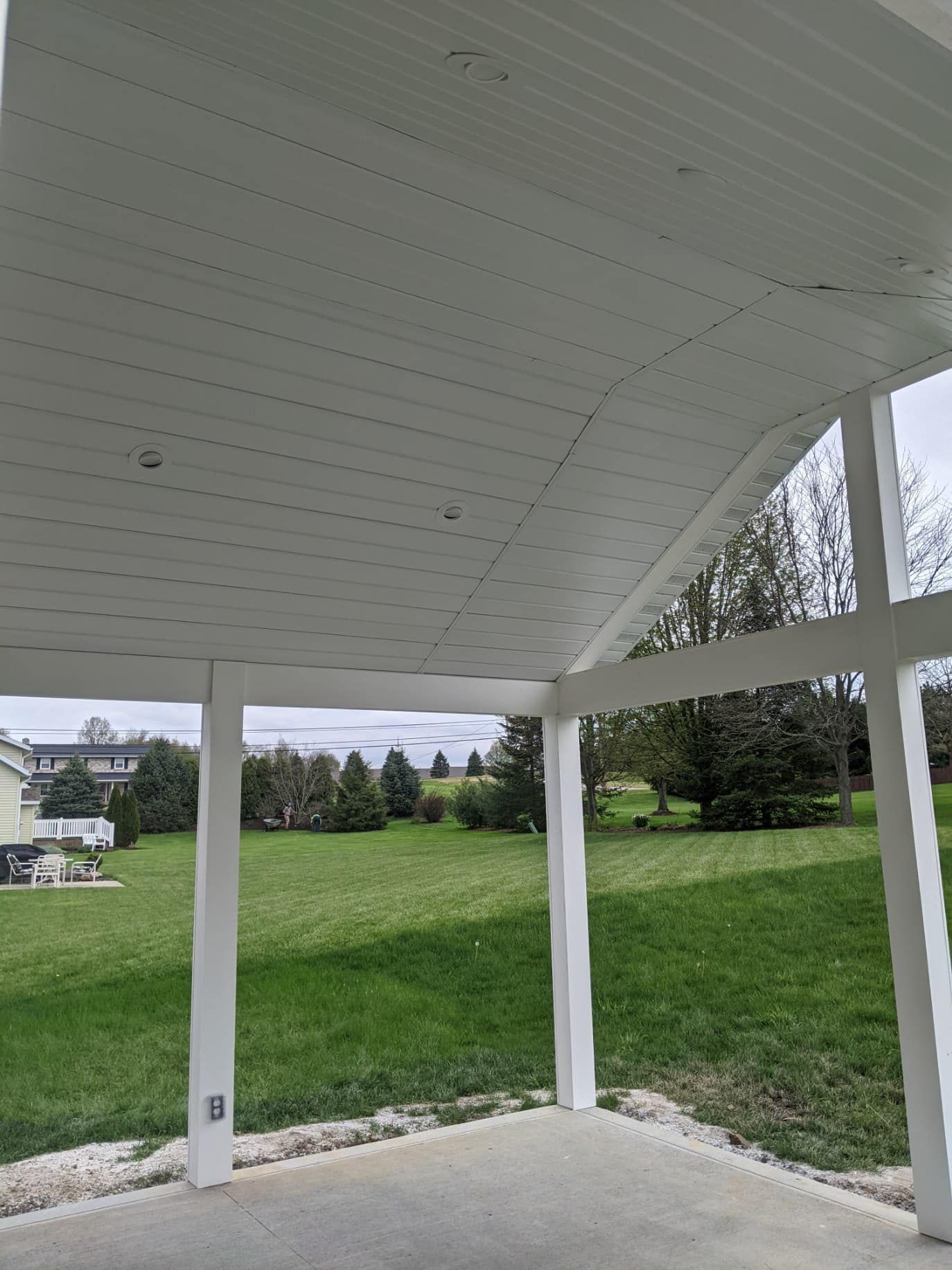White porch with a view of a green lawn and trees under an overcast sky.