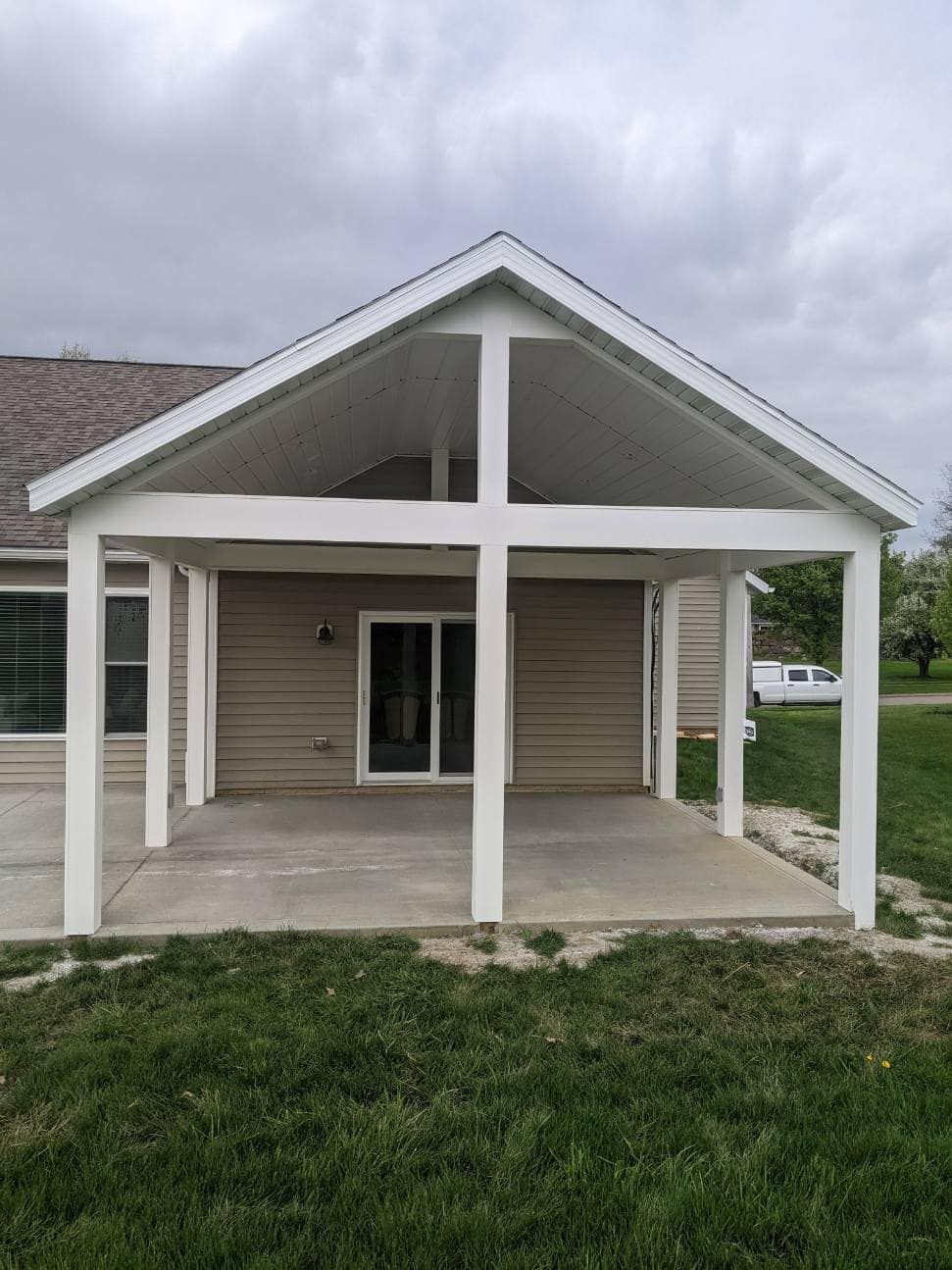 Covered patio with white frame, concrete floor, and sliding glass door, under overcast sky.