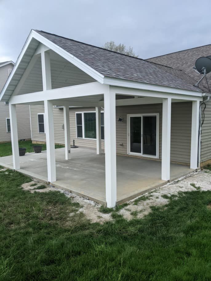 White-framed patio cover attached to a house with a concrete floor, set on green grass.
