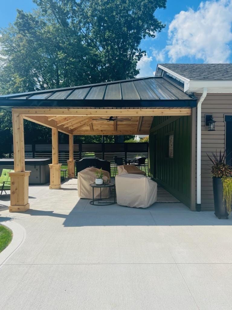 Patio with wooden pergola and metal roof, two covered chairs, and concrete flooring.