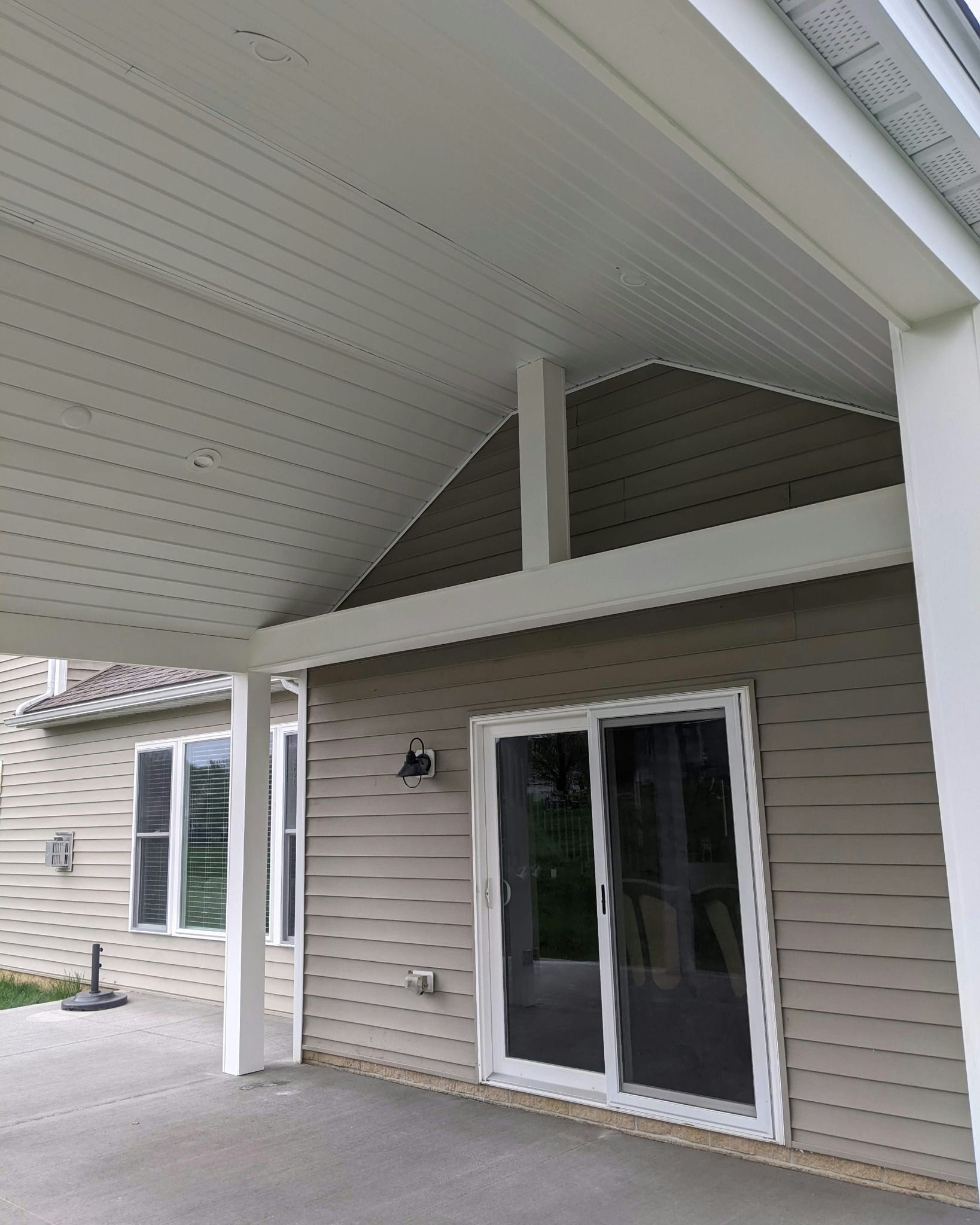Covered patio with white pillars and ceiling. Sliding glass door and tan siding.