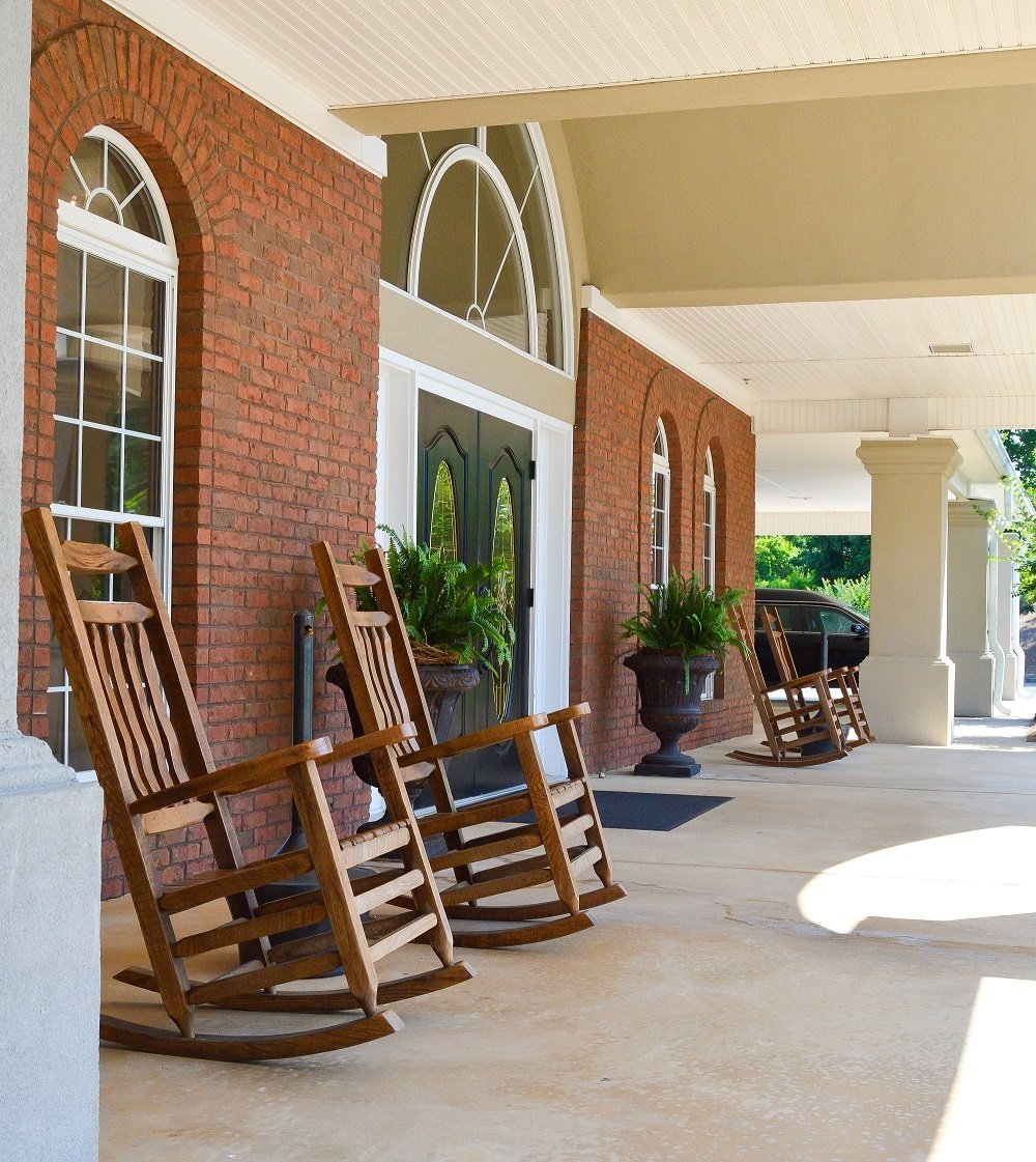 A row of rocking chairs on a porch in front of a brick building
