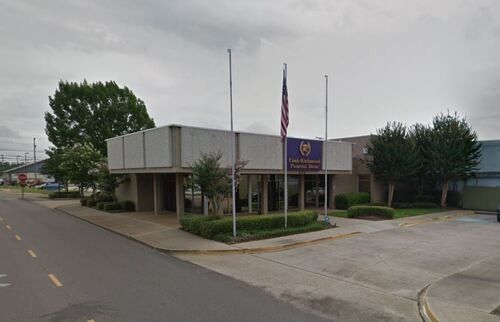 Exterior view of a one-story, beige building with the American flag and a sign reading 