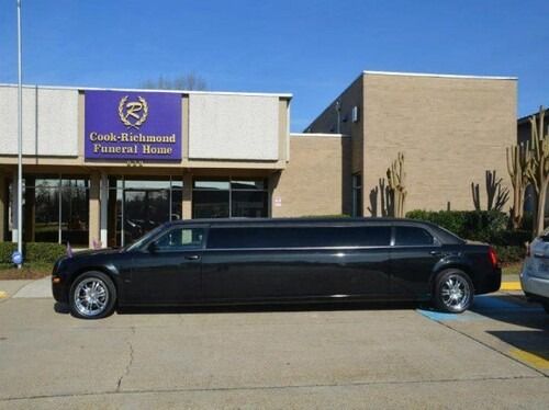 Black limousine parked in front of a funeral home with a purple and gold sign.