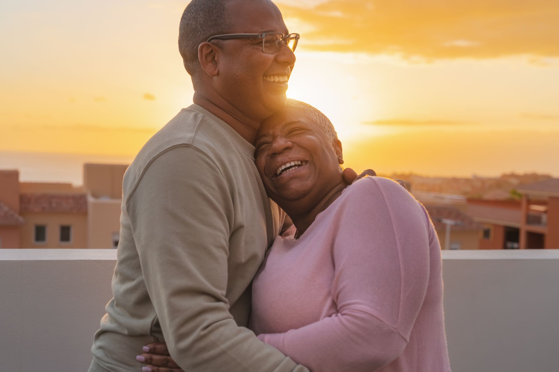 Couple embracing, smiling, silhouetted by golden sunset on rooftop.