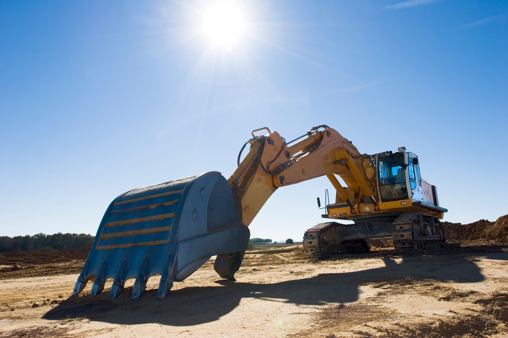 A large yellow excavator is sitting on top of a dirt hill.