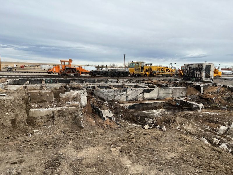 Demolished building foundation next to railroad tracks; machinery on rails; overcast sky.